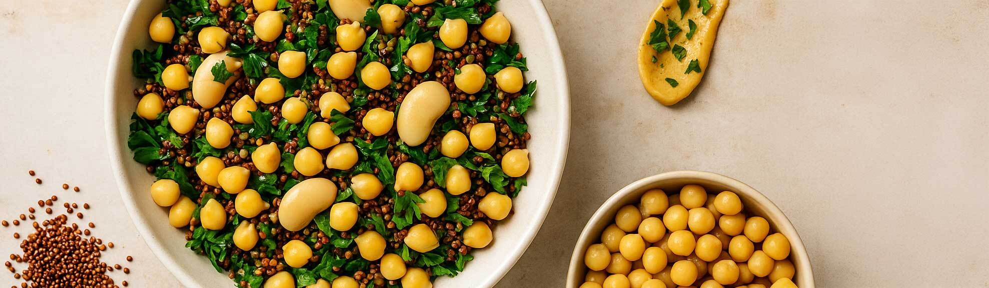 Protein-rich chickpea and red quinoa salad with butter beans, hummus, and fresh parsley, shown in a ceramic bowl with scattered ingredients on a neutral background – high-protein plant-based meal idea.