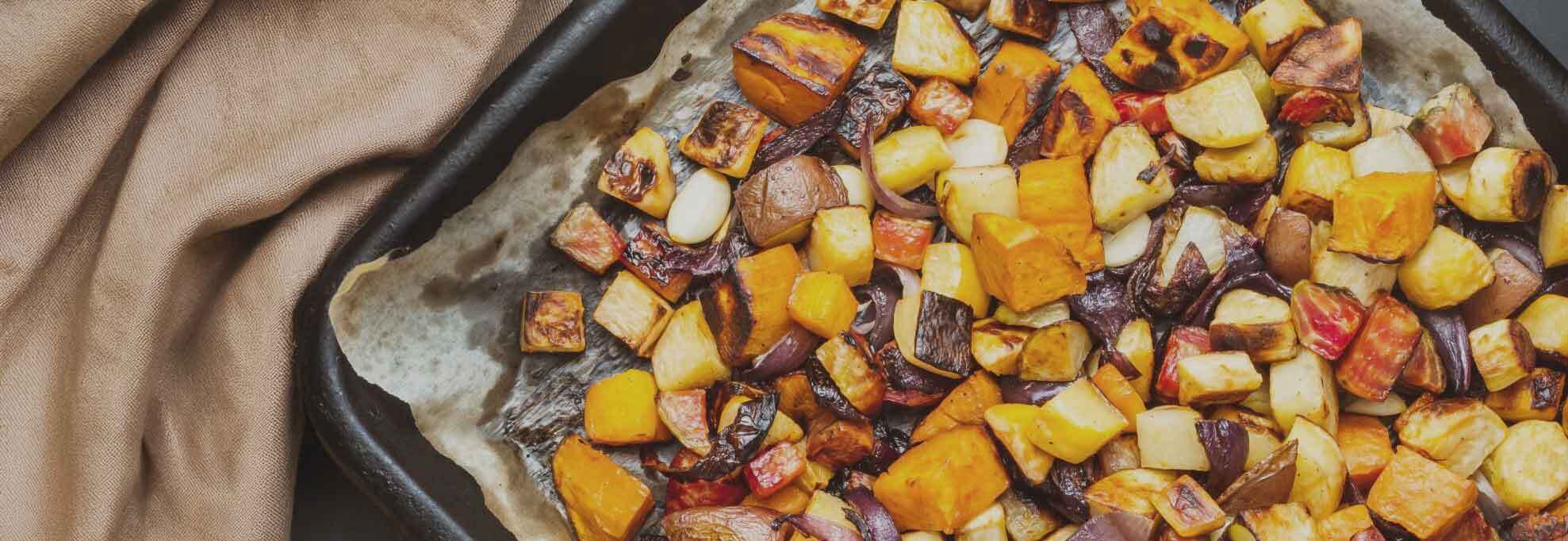 Tray of roasted root vegetables including carrots, parsnips, potatoes and red onion, perfect for drizzling with Roquito Hot Honey