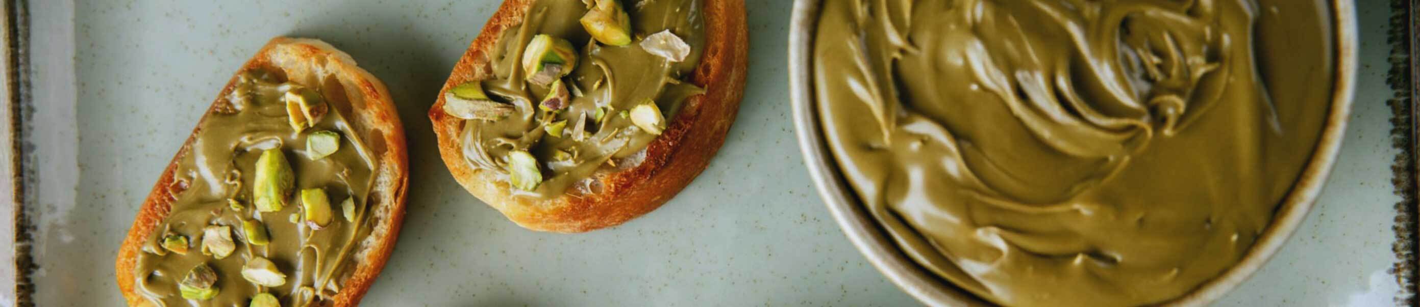 Pistachio compound paste in a white bowl with pistachio paste on biscuits