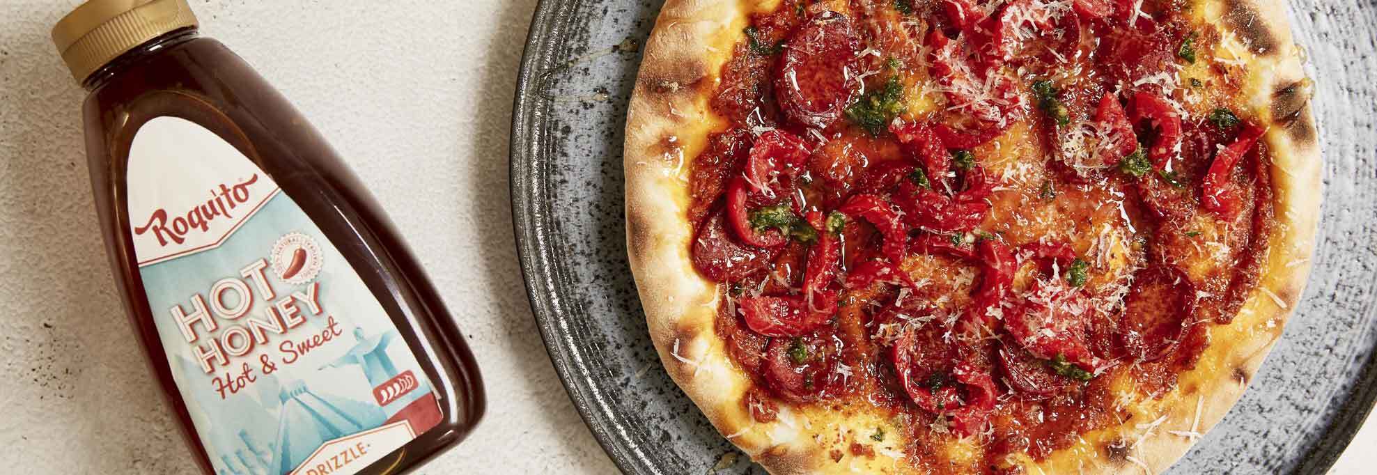 Bottle of Roquito Hot Honey with spicy pepperoni pizza drizzled in hot honey on a rustic plate.